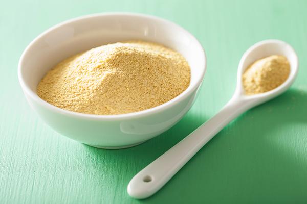 Nutritional yeast in a bowl next to a spoon.