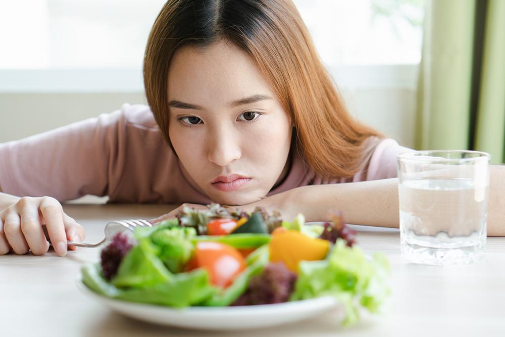 Asian female teen looking at a plate of salad.