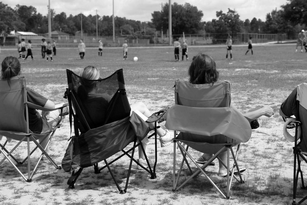 Parents sitting in chairs on sideline of child's sports game.