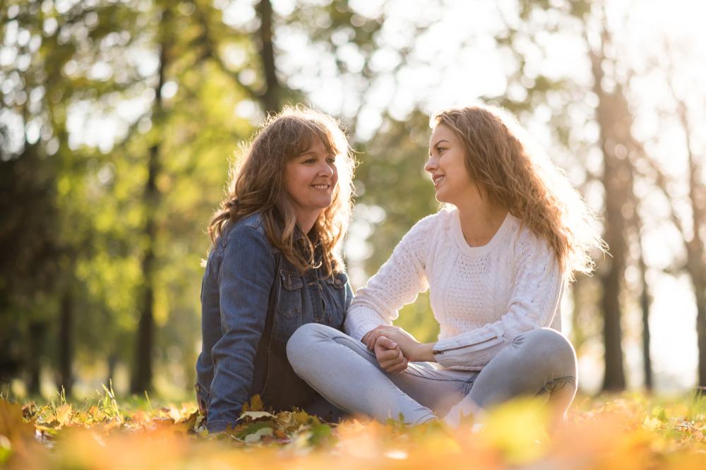 Mother sitting with teen daughter outside.