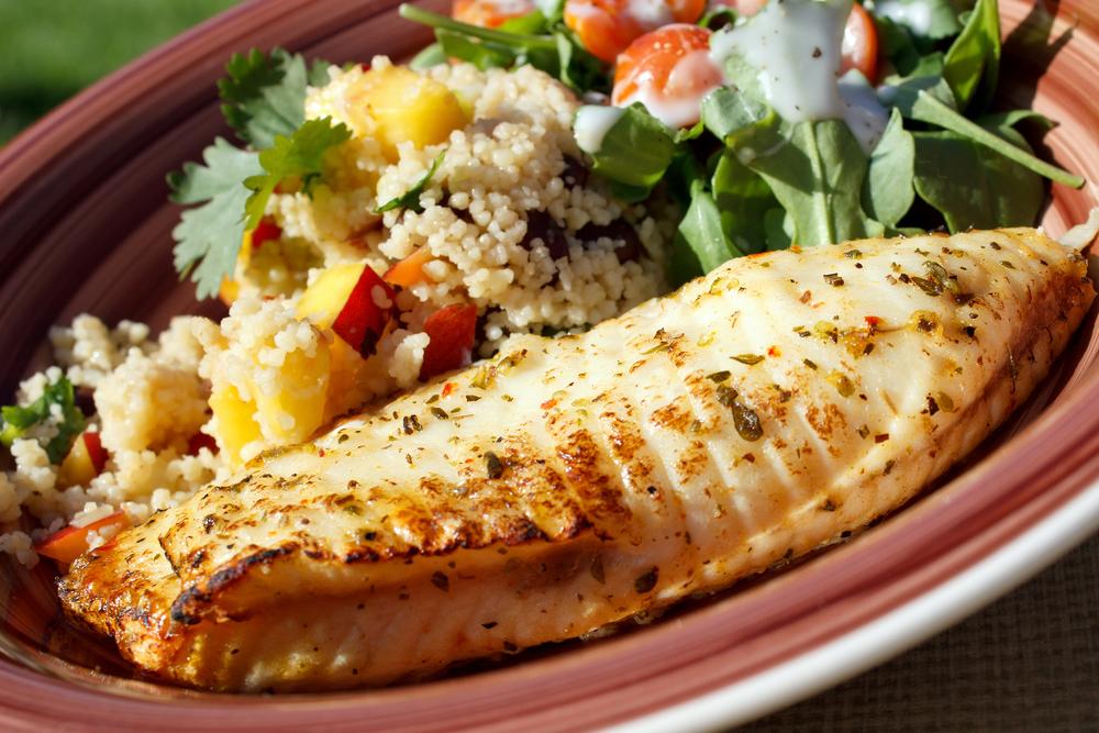 Grilled tilapia next to vegetable quinoa.