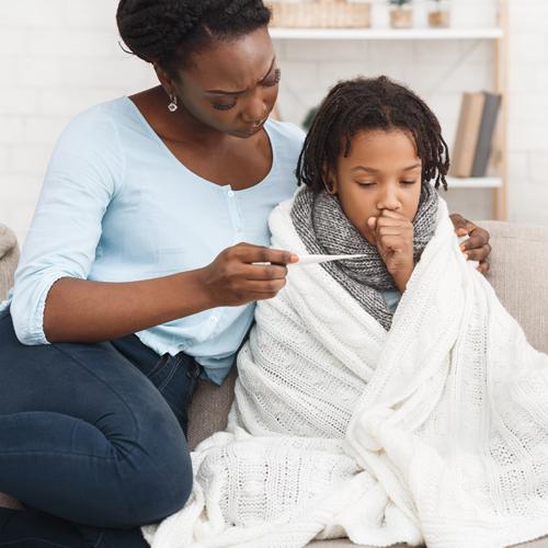 Black mother comforting sick child while looking at thermometer.