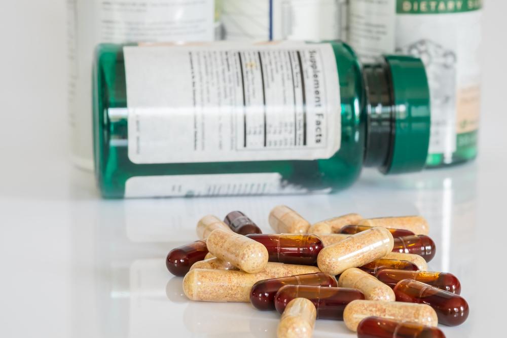 Pile of supplements pills next to a bottle on it's side.