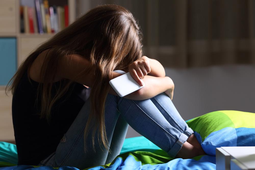 Girl holding phone with her head on her knees.