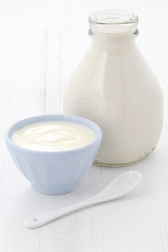 Glass of milk next to a bowl of yogurt and a spoon.