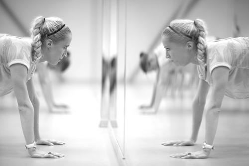 Young white woman doing a pushup while looking in the mirror.