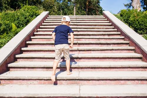 Barefoot young white male child going up stairs outdoors.