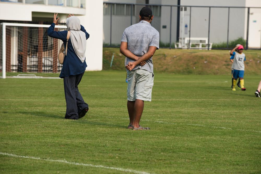 Two parents looking frustrated on the sidelines of a youth soccer game.