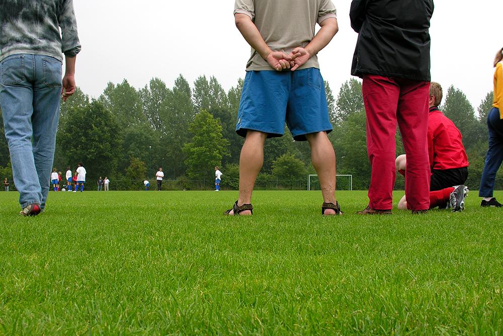 Parents standin on sideline at soccer game.