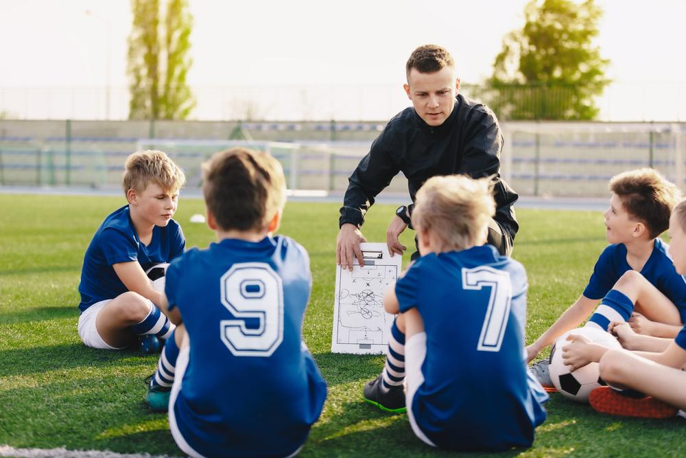 Male coach sharing game plan with young male soccer team.