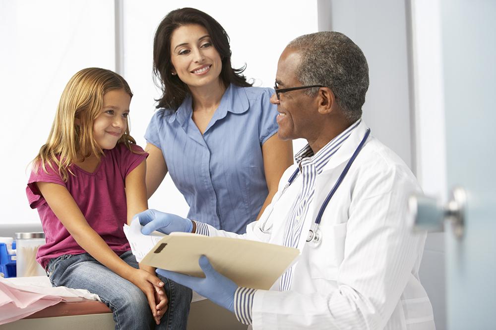 Black doctor talking to white girl and her mom in office.