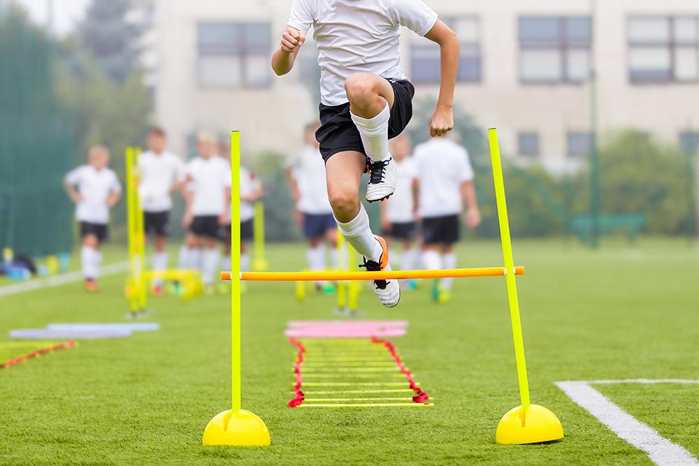 Teen male training by jumping over hurdle.