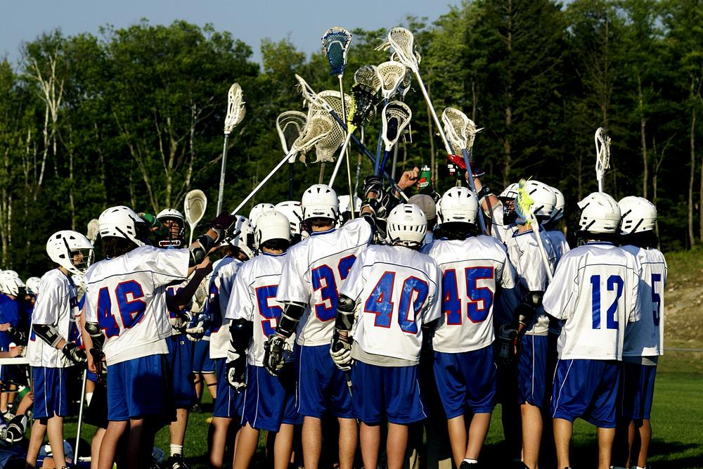 Lacrosse team huddled with sticks in the air.