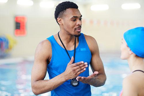 Adult make swim coach talking to young female swimmer.