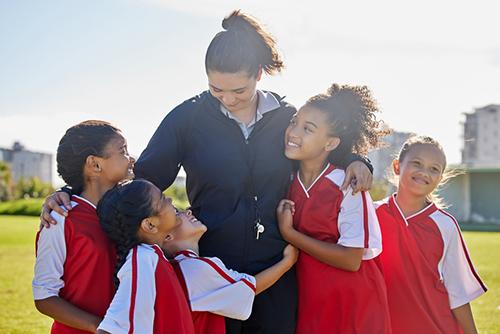 Woman coach of young female soccer team smiling and hugging.