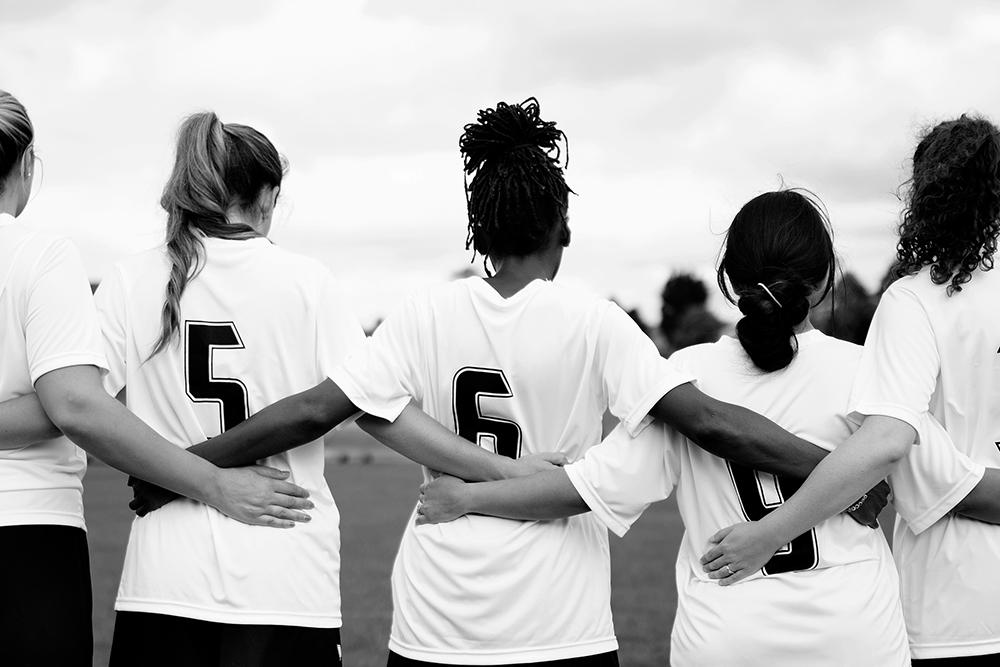 Diverse teen girl sports team linking arms.