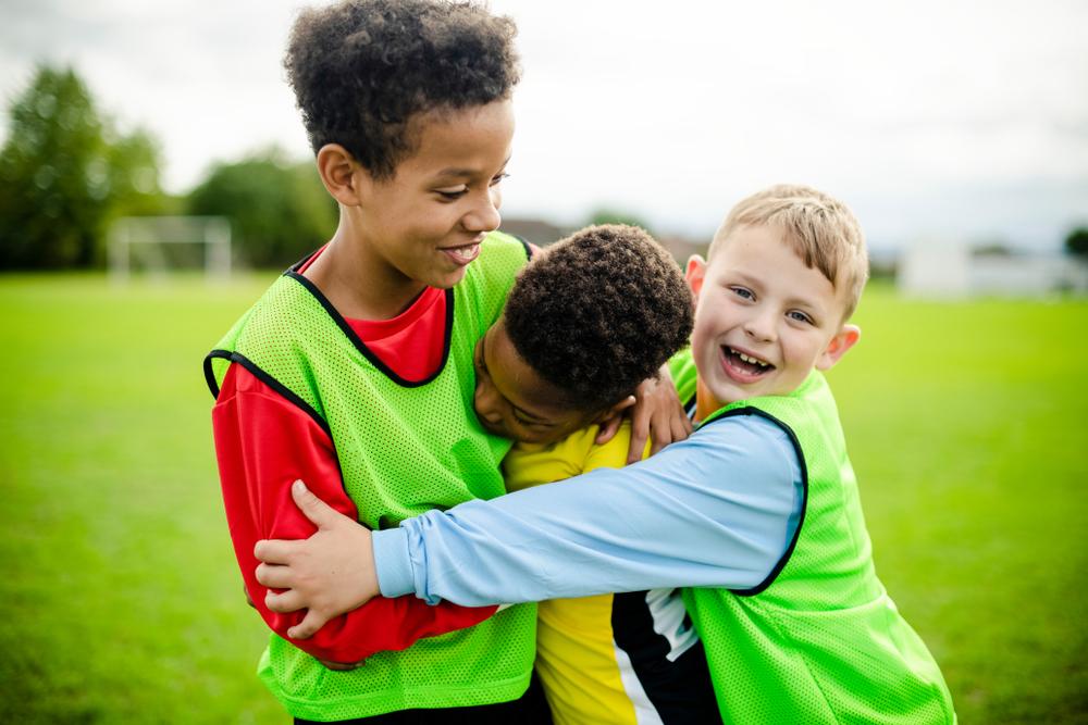 Three diverse young male teammates hugging.