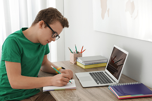 Teen boy writing in notebook.