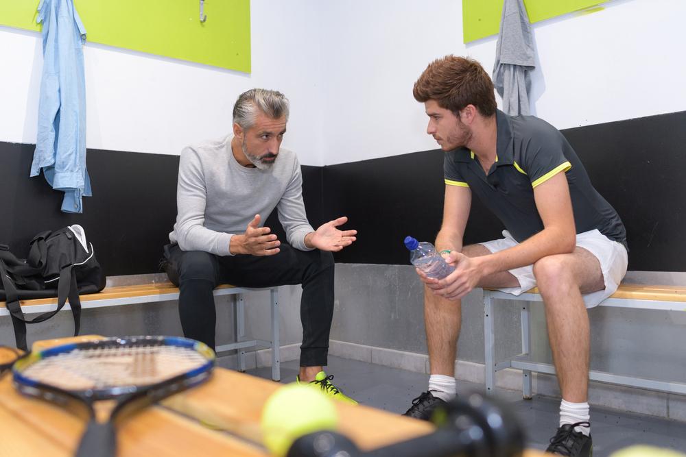 Tennis coach talking to young male athlete in locker room.