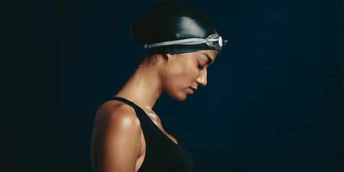 Female swimming looking down against dark background.