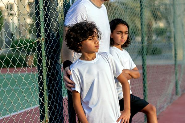 Two upset youth athletes on sidelines of tennis court with coach.