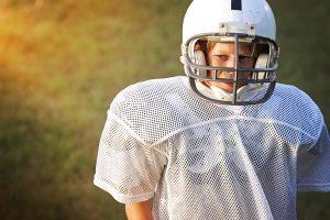 Young white football player standing alone looking upset.