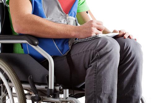 close up of young man in wheelchair writing on a note pad.