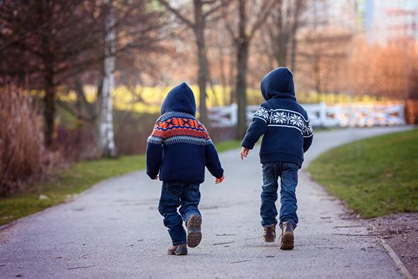 A rear view of two young boys wearing winter hoodies walking down a path.