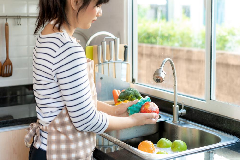 Asian woman washing fruit in sink.