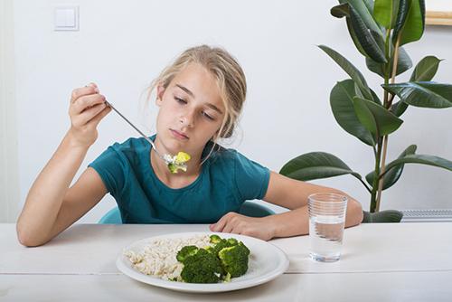 Teen girl holding up a fork of food looking disappointed.