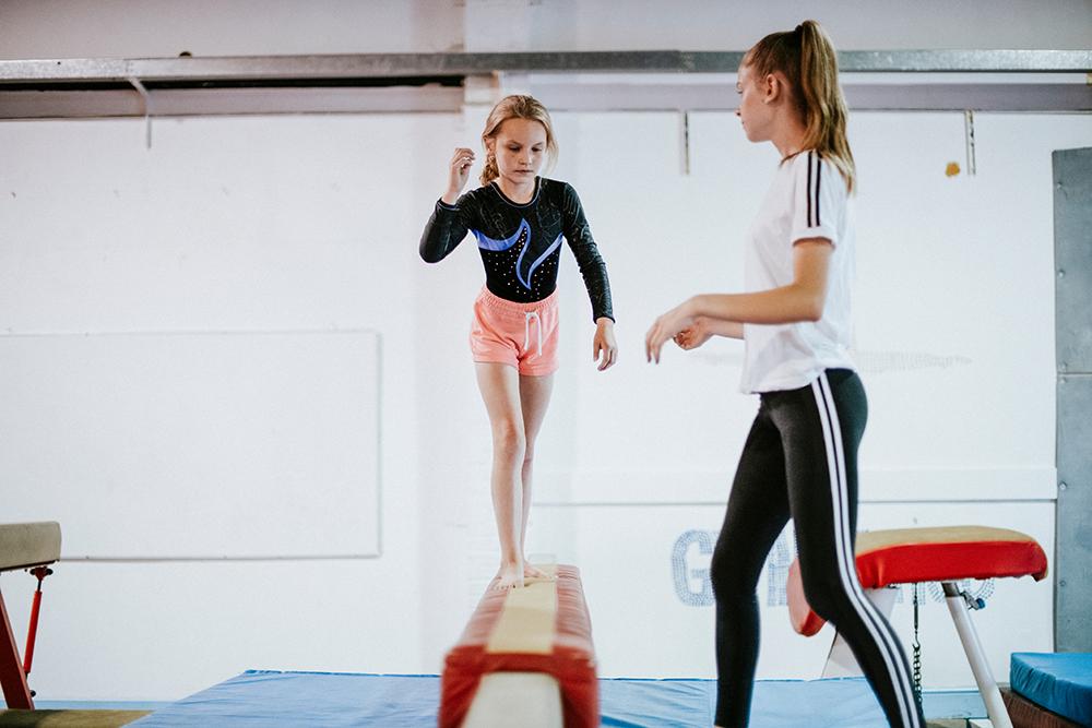 Young female gymnast training on balance beam.